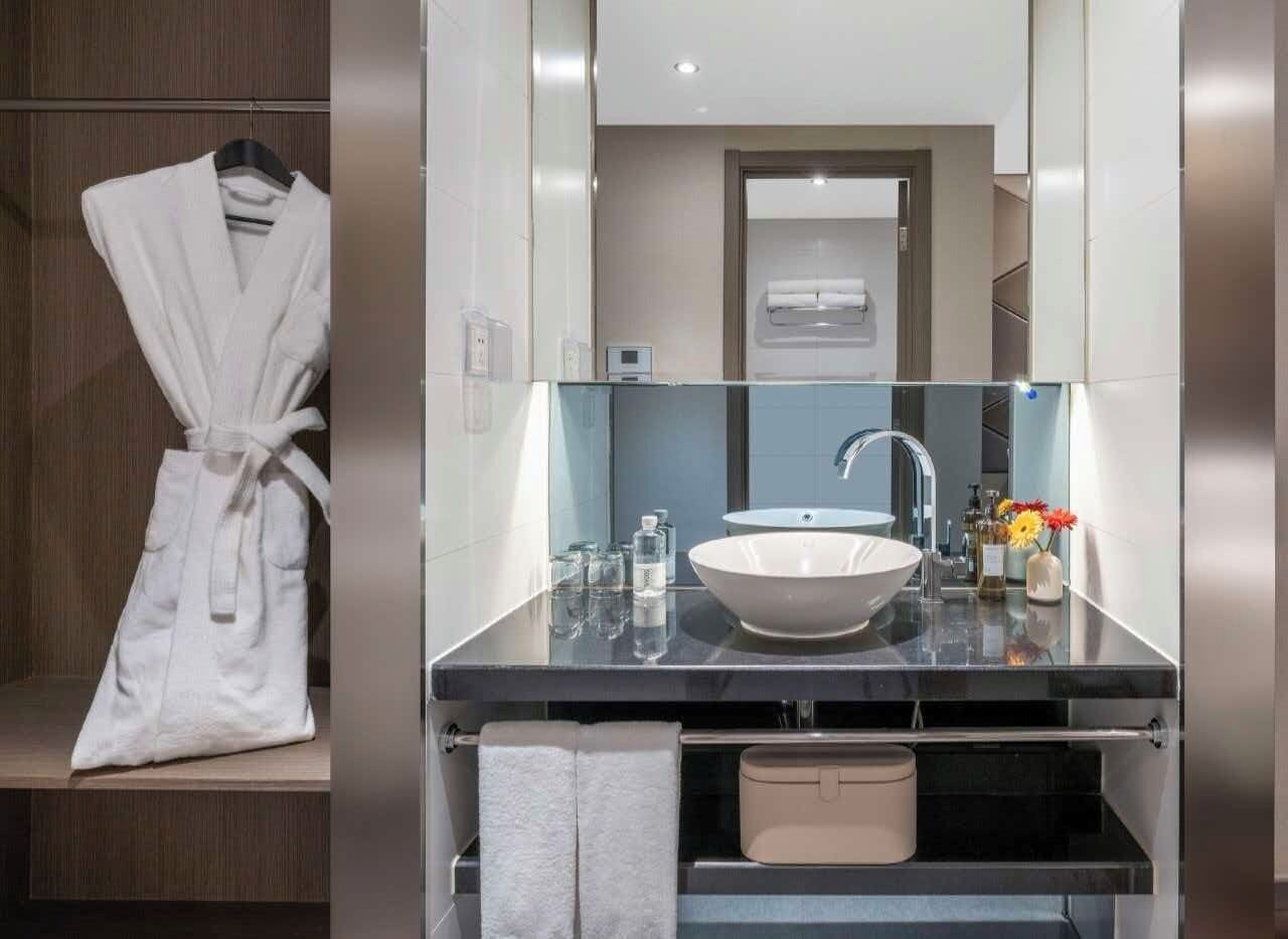 A modern bathroom with a large mirror, a white sink, and a robe hanging on a rack.