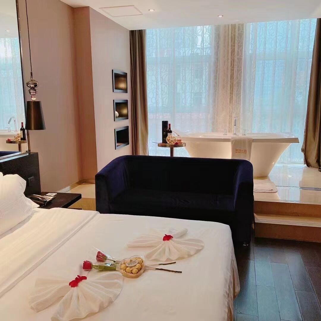 A hotel room with a large bed, a sitting area, a bathtub, and a window with curtains.