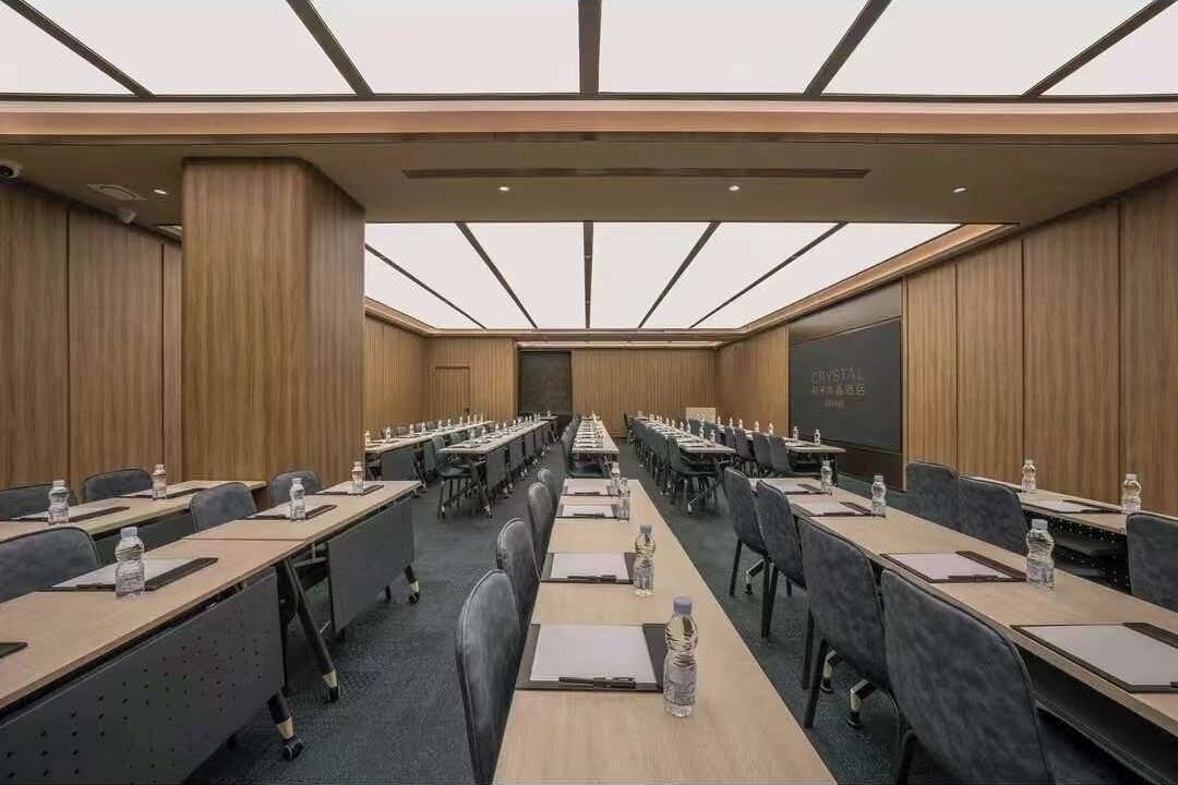 Un salón de conferencias con largas mesas, sillas y una pantalla de proyector.
