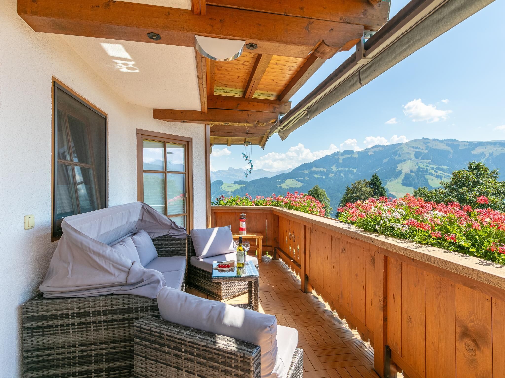 A balcony with wicker furniture, a table with a bottle, and a view of mountains.