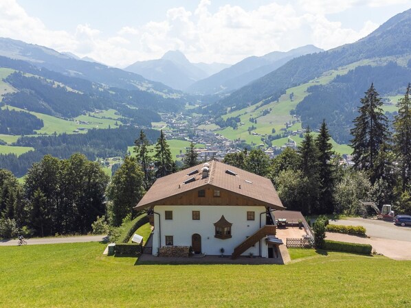 Un edificio blanco con techo inclinado, rodeado de un paisaje verde y montañas al fondo.