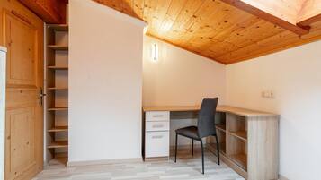 A room with a wooden ceiling, a desk with a chair, a wardrobe, and a built-in shelving unit.