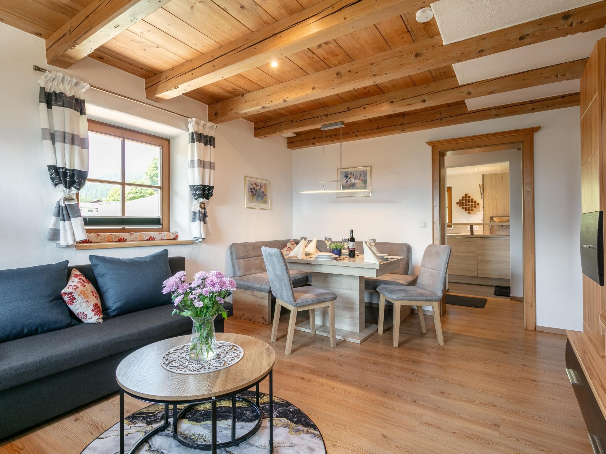 Een gezellige woonkamer met een bank, een bijzettafeltje met een bloevas en een eethoek met stoelen en een tafel.