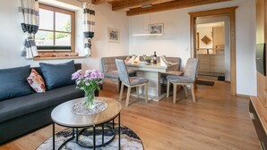 En hyggelig stue med en sofa, et sofabord med en vase blomster og et spiseområde med stole og et bord.
