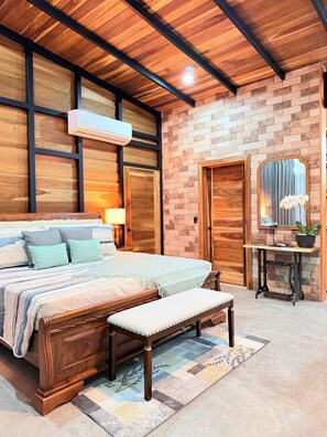 A bedroom with a wooden bed, a bench, a nightstand, a mirror, and a potted plant. - Cabaña privada con jacuzzi en La Fortuna, Cerca del Volcan Arenal y Catarata. (Alajuela)