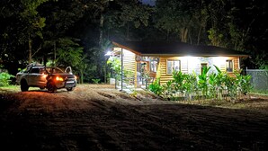 Une maison en bois à deux étages, dotée d’un porche et entourée d’une végétation luxuriante.