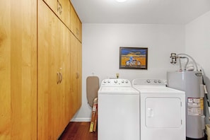 A laundry room with wooden cabinets, a washing machine, a dryer, and a water heater.