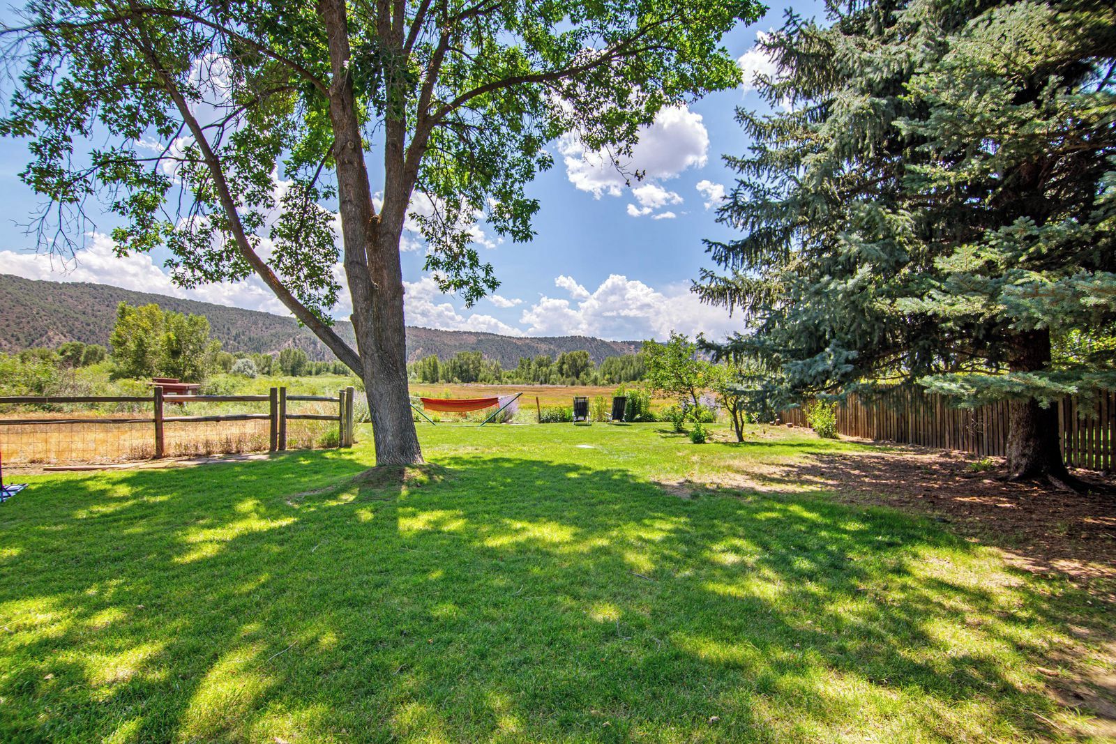 A fenced outdoor area with a hammock, trees, and a view of distant hills.