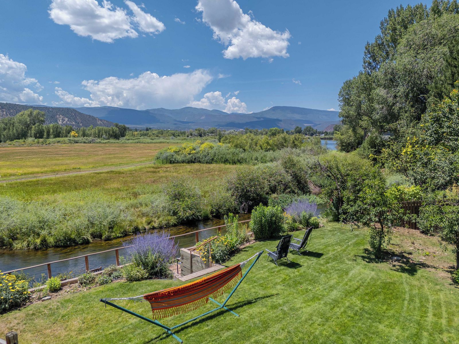 A grassy area with a hammock, chairs, and a river.