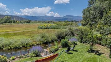 A grassy area with a hammock, chairs, and a river.