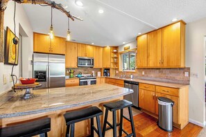 A modern kitchen with wooden cabinets, stainless steel appliances, a granite countertop, and pendant lighting.