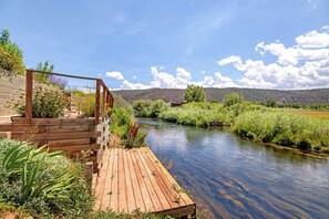A wooden deck overlooking a river with a view of a forested hillside.