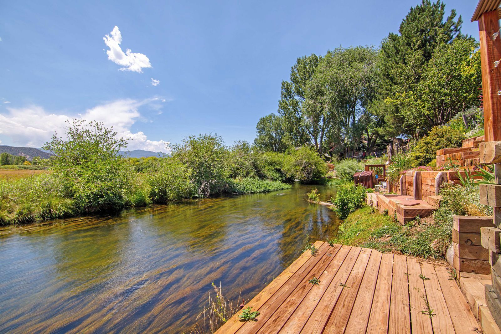 A wooden deck overlooking a river with a natural landscape and a building with rustic wooden structures.