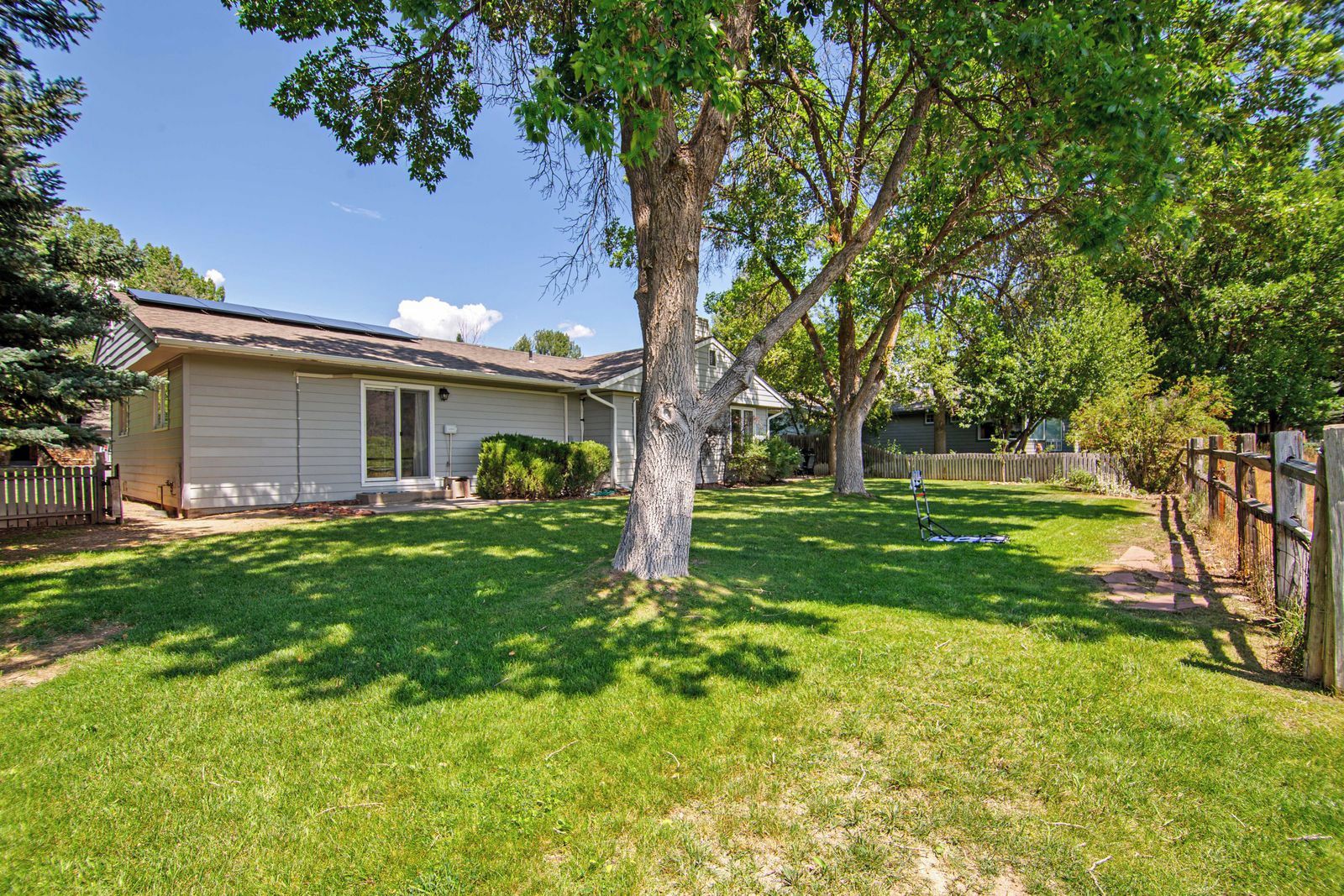 A residential property with a detached house, a fenced yard, and a large tree.