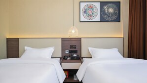 Een hotelkamer met twee bedden, een nachtkastje met een klok en een telefoon, en een kunstwerk aan de muur.