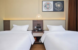 A hotel room with two beds, a nightstand with a clock and a phone, and a wall-mounted artwork.