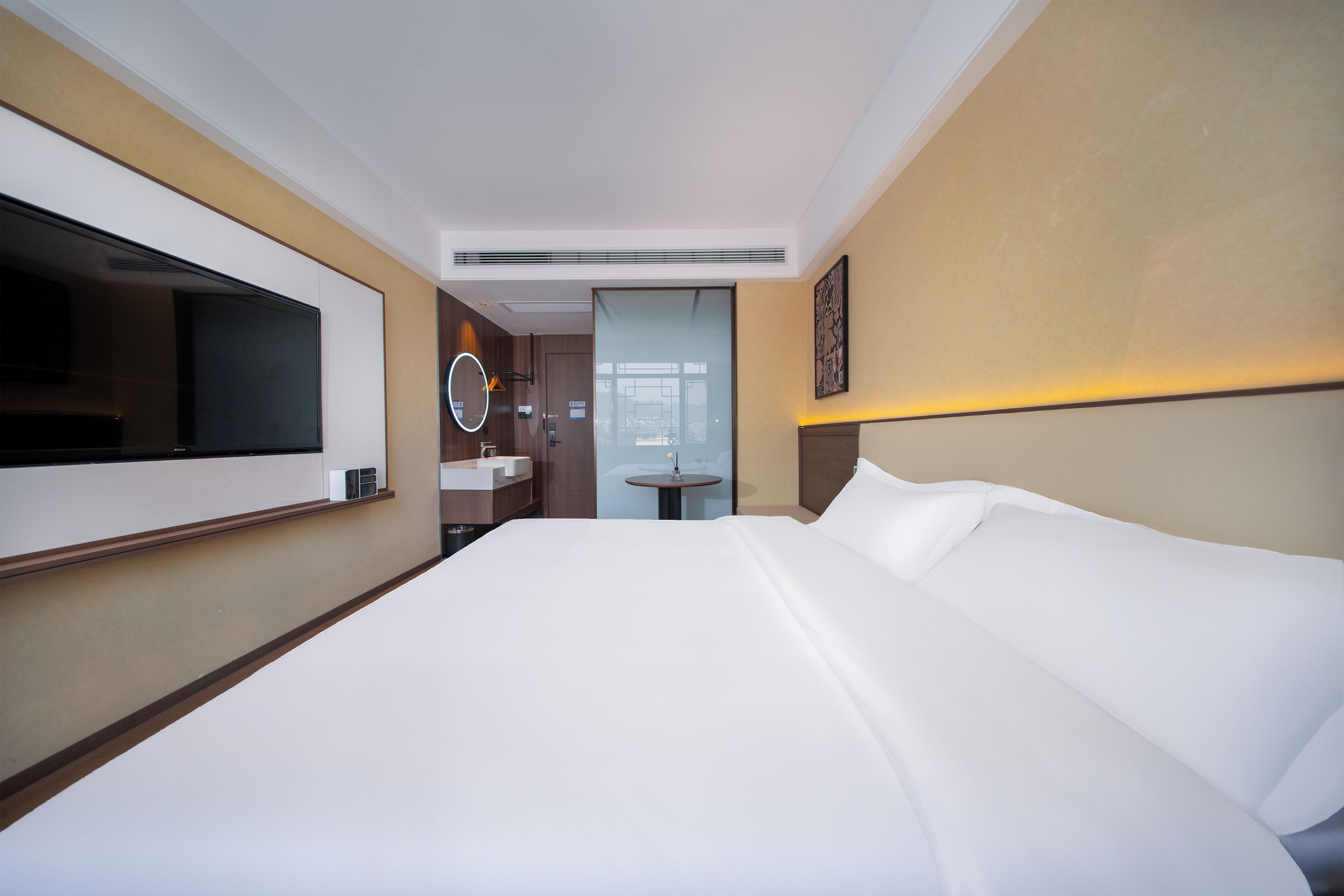 Habitación de hotel con una cama grande, televisión, baño con lavamanos y espejo, y vista a la ciudad desde la ventana.