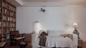 Uma sala de estar com um sofá, uma poltrona, uma mesinha, uma estante e um abajur.