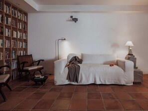 Een woonkamer met een bank, een stoel, een bijzettafeltje, een boekenkast en een lamp.