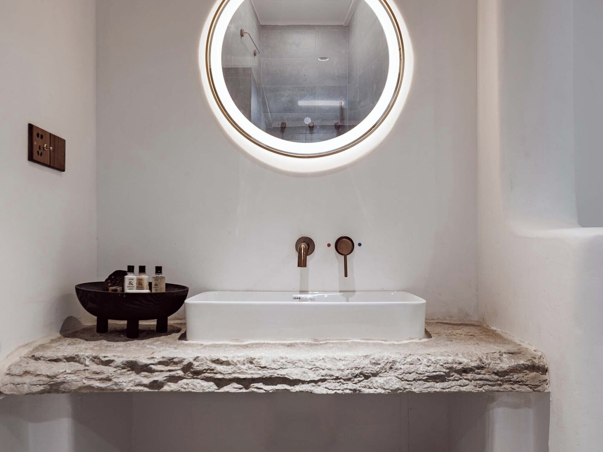 A bathroom with a white sink, a round mirror, and a black basin on the countertop.