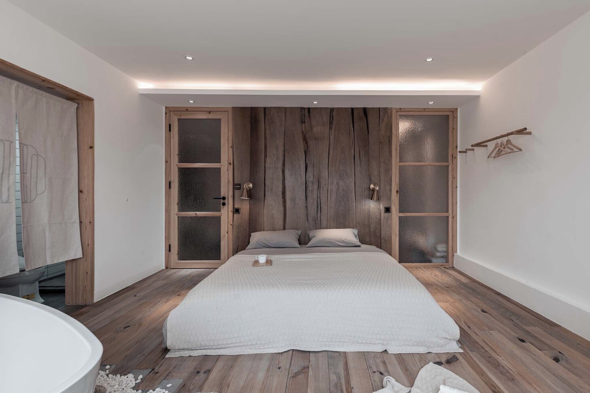 A bedroom with a large bed, wooden flooring, and a modern design.