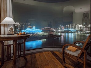 A room with a view of a cityscape at night, a table with a lamp, and a chair with a cushion. - Boys2men (Chongqing)