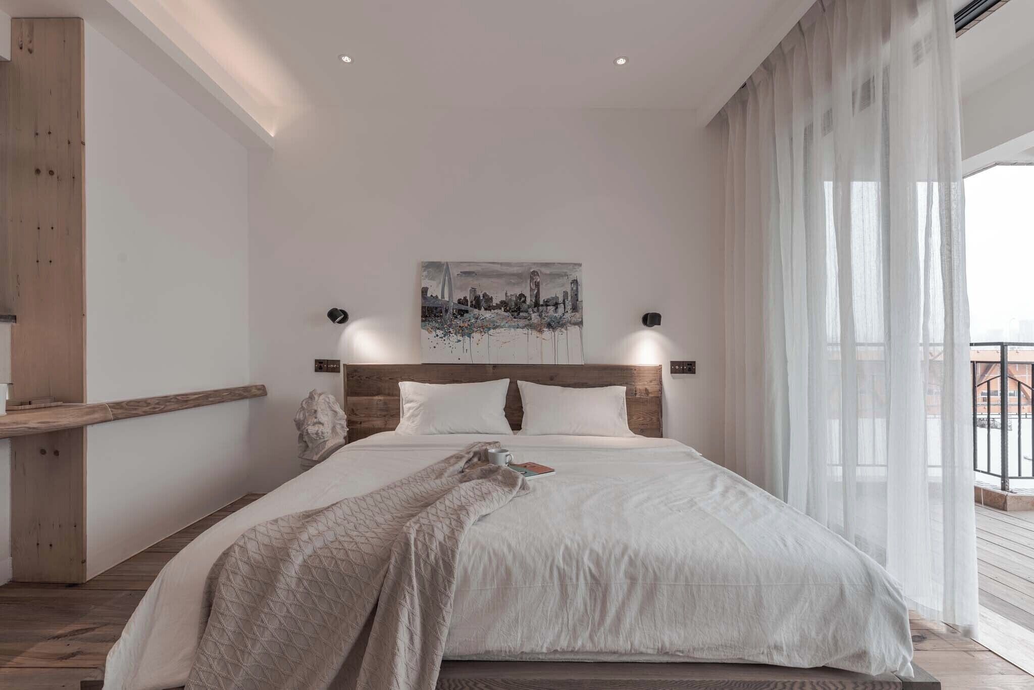 Un dormitorio moderno con una cama grande, un cuadro de un paisaje urbano y un balcón con cortinas.