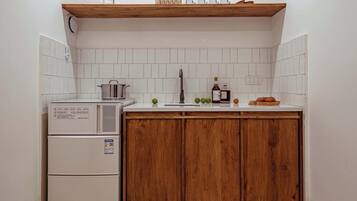 Cocina compacta con refrigerador integrado, un gabinete de madera, un lavamanos y un estante sobre la encimera.