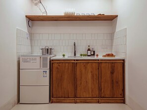 Cocina compacta con refrigerador integrado, un gabinete de madera, un lavamanos y un estante sobre la encimera.