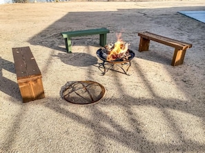 A sandy outdoor area with a fire pit, two benches, and a metal grill. - Charming 3-bedroom house with AC in serene Joshua Tree (Joshua Tree)