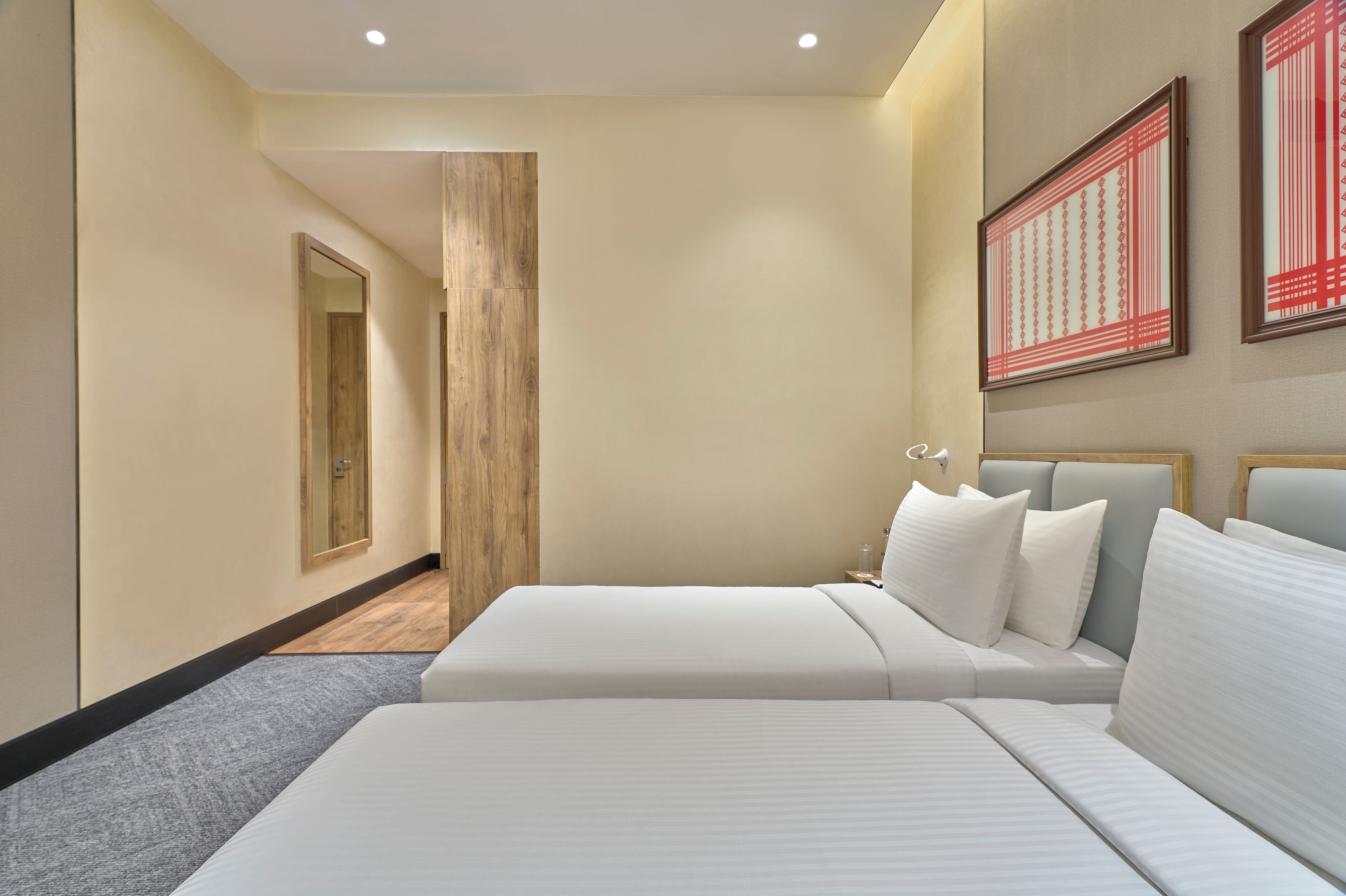Quarto de hotel com duas camas, uma porta de madeira e parede decorada com molduras.