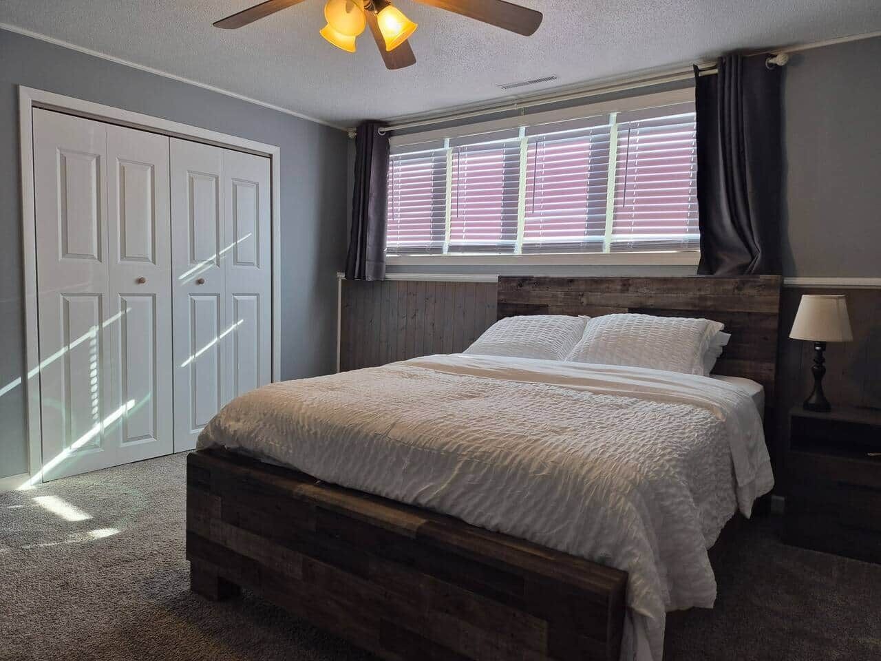 A bedroom with a bed, a ceiling fan, a window with blinds, and a door.
