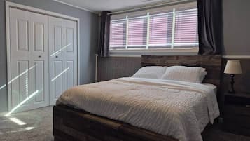 A bedroom with a bed, a ceiling fan, a window with blinds, and a door.