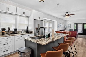 A modern kitchen with white cabinetry, a marble countertop, a stainless steel refrigerator, and a bar area with leather stools. - Spacious home ft. backyard with exclusive hot tub! (Louisville)