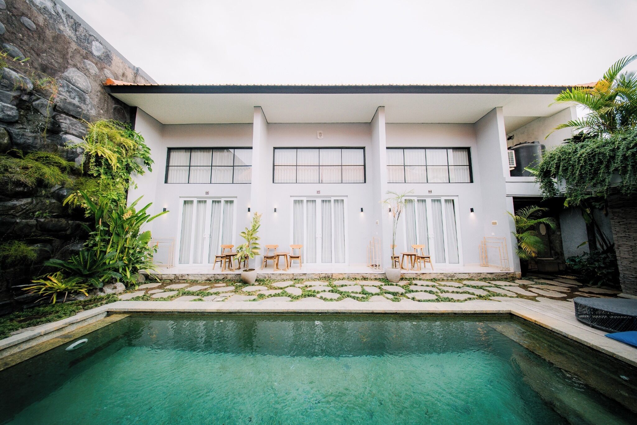 A modern building with a pool, outdoor seating, and lush greenery.