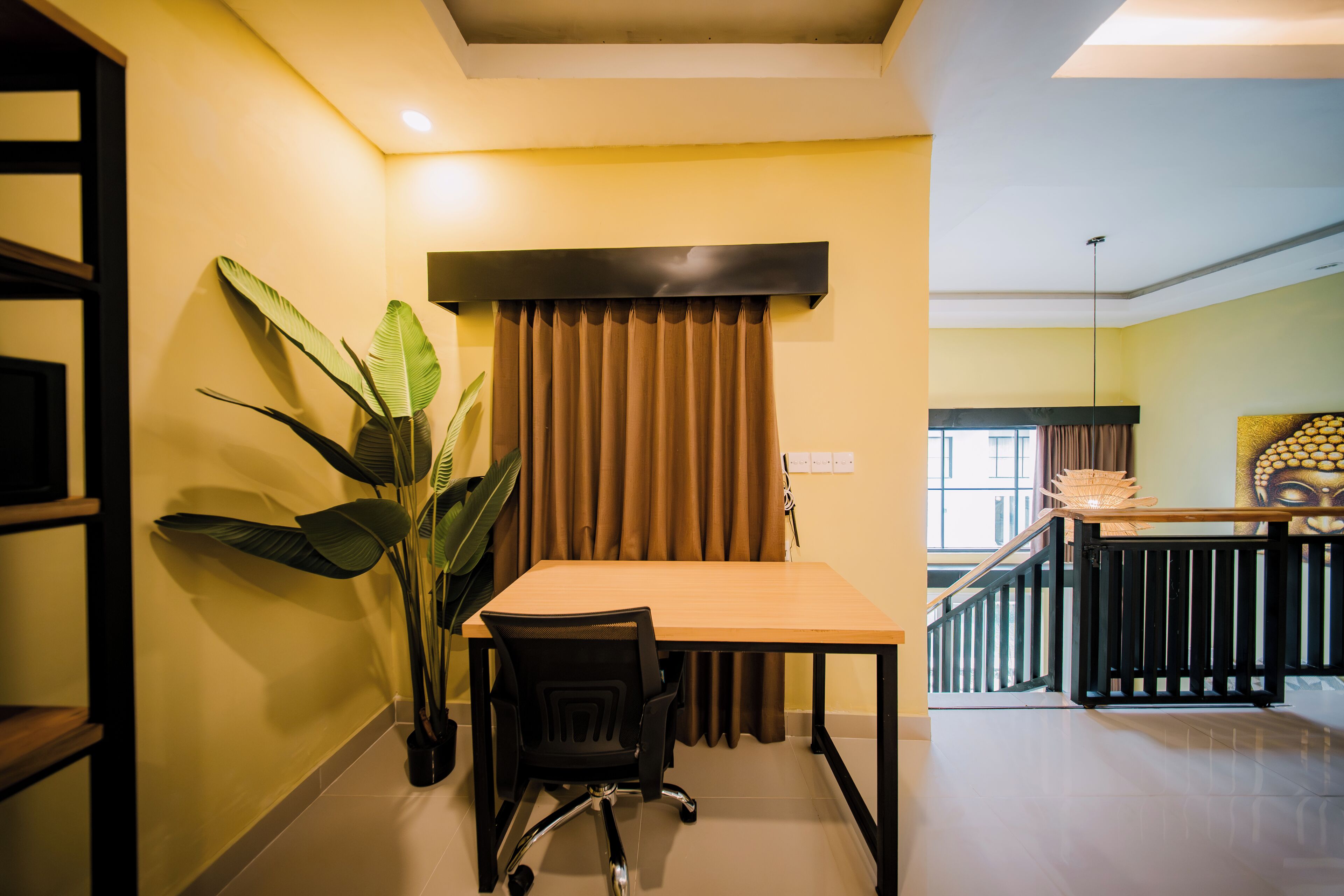 Una habitación con una mesa, sillas, una planta en maceta, una ventana con cortinas y una escalera que sube a otro nivel.