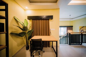 Una habitación con una mesa, sillas, una planta en maceta, una ventana con cortinas y una escalera que sube a otro nivel.