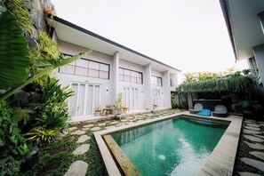 Ein modernes Haus mit Pool, Sitzgelegenheit im Freien und üppiger Bepflanzung.