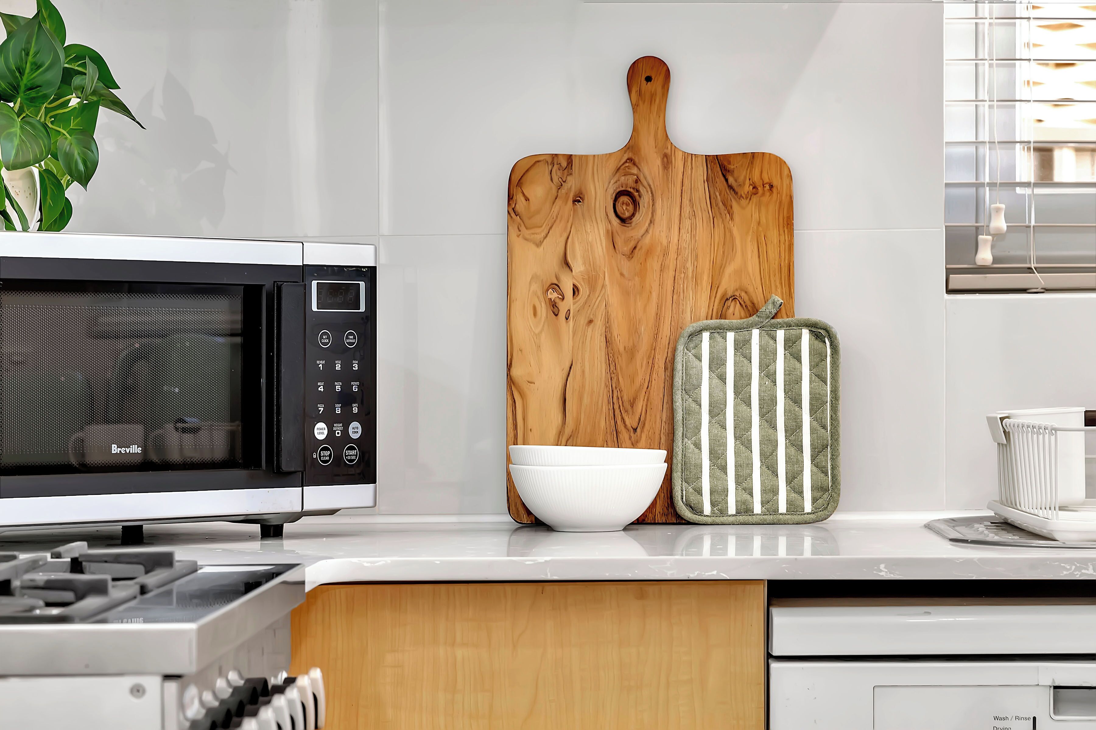 Una cocina con un microondas Breville, una tabla de cortar de madera, un bol blanco y un agarrador de olla a rayas verde y blanco.