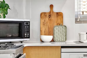 Una cocina con un microondas Breville, una tabla de cortar de madera, un bol blanco y un agarrador de olla a rayas verde y blanco.
