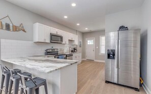 A modern kitchen with white cabinets, a marble island, and stainless steel appliances.