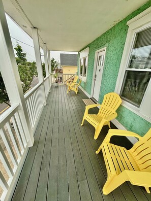 A covered porch with wooden flooring, yellow chairs, and a green wall.