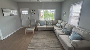A living room with a beige sectional sofa, a wooden chair, a small table, a ceiling fan, and a view of the outdoors through a window. - Sleeps 15, 5BR, 2 Blocks to Convention Center & Beach, 2 Parking Spots (Wildwood)