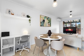 A modern living room with a white sofa, a round dining table with chairs, a TV displaying 'NETFLIX', and a wall-mounted shelf with decorative items. - The Finch Fern A Sepal Stay (Perth)