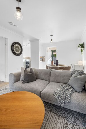 A modern living room with a sectional sofa, a wooden coffee table, and a dining area with a table and chairs. - The Finch Fern A Sepal Stay (Perth)
