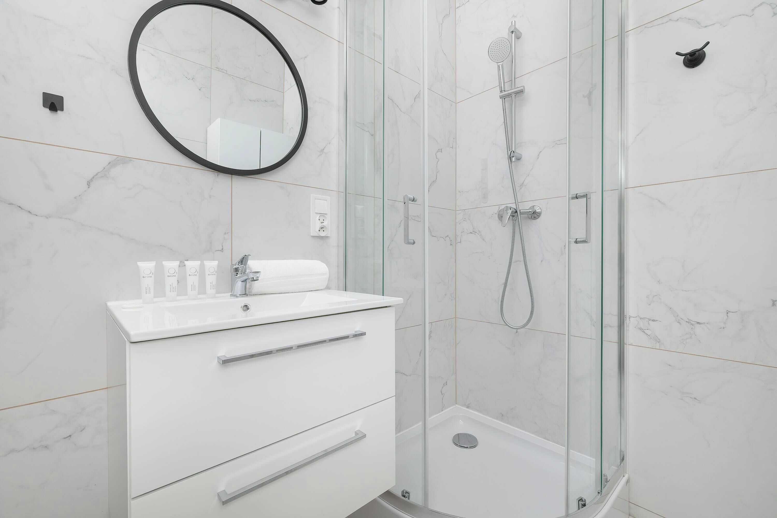 Un baño moderno con tocador blanco, espejo redondo y cabina de ducha con mampara de vidrio.