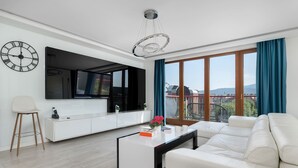 A modern living room with a white sofa, a coffee table, a TV, and a large window with curtains. - Stylish Apartment with a Balcony | Close to City Center (Bielsko-Biała)
