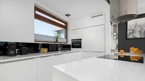 A modern kitchen with white cabinetry, a large island, and a cityscape painting. - Stylish Apartment with a Balcony | Close to City Center (Bielsko-Biała)