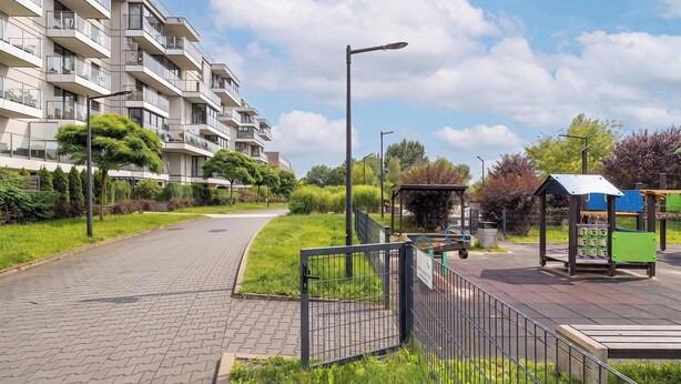 Ein Wohngebäude mit mehreren Balkonen, einem gepflasterten Weg und einem Spielplatz mit einem Pavillon.