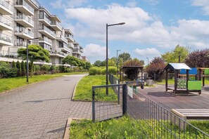 Ein Wohngebäude mit mehreren Balkonen, einem gepflasterten Weg und einem Spielplatz mit einem Pavillon.